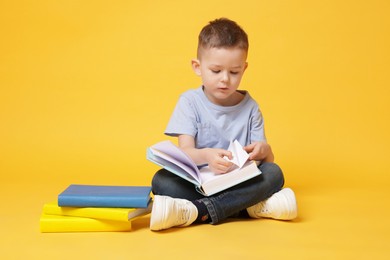 Photo of Cute little boy reading book on yellow background
