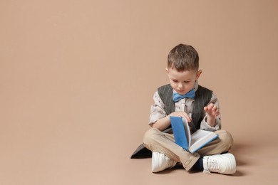 Photo of Cute little boy reading book on beige background, space for text