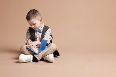 Photo of Cute little boy reading book on beige background, space for text