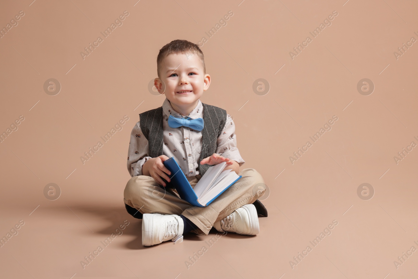 Cute little boy with book on beige background Photo of Cute little boy with book on beige background