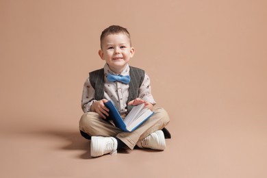 Photo of Cute little boy with book on beige background