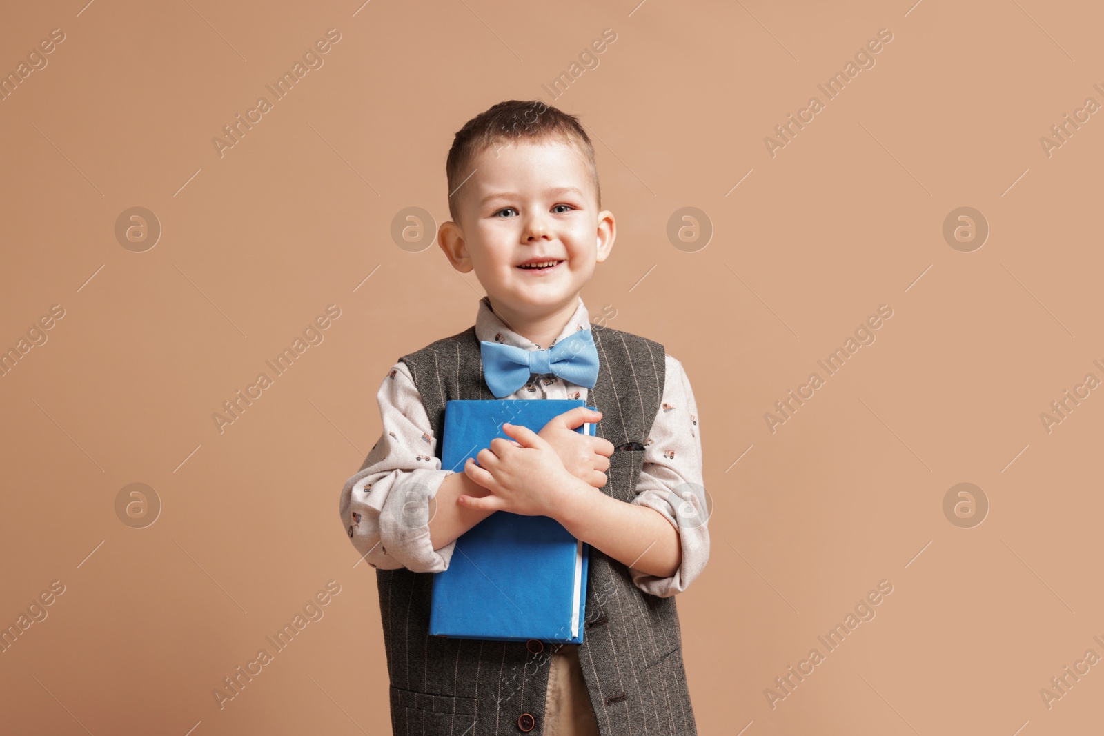 Cute little boy with book on beige background Photo of Cute little boy with book on beige background
