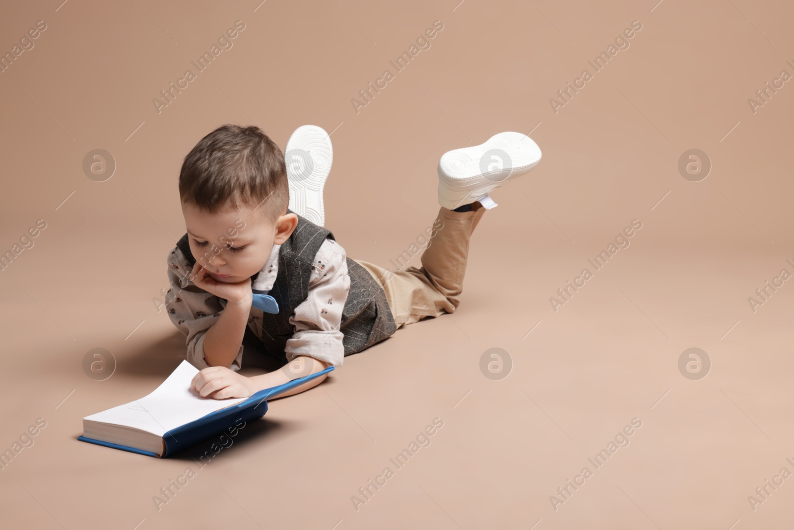 Cute little boy reading book on beige background Photo of Cute little boy reading book on beige background