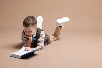 Photo of Cute little boy reading book on beige background