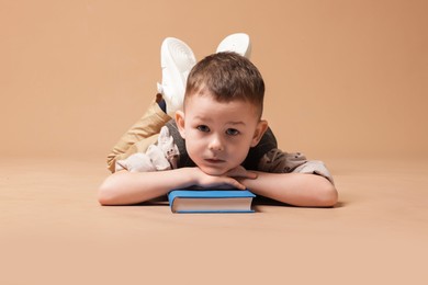 Photo of Cute little boy with book on beige background