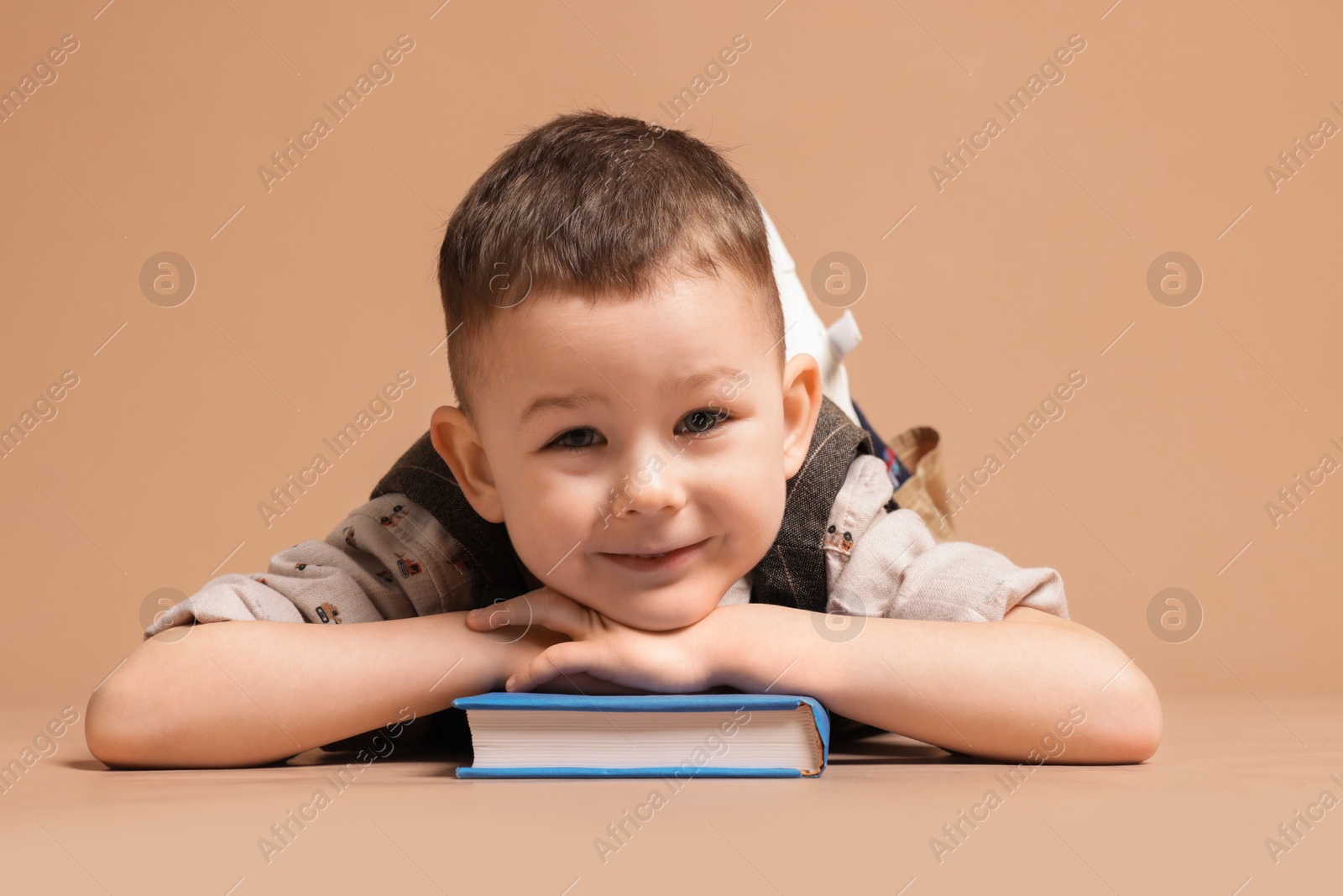 Cute little boy with book on beige background Photo of Cute little boy with book on beige background
