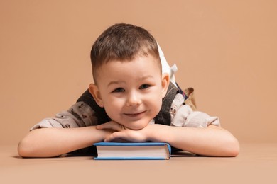 Photo of Cute little boy with book on beige background