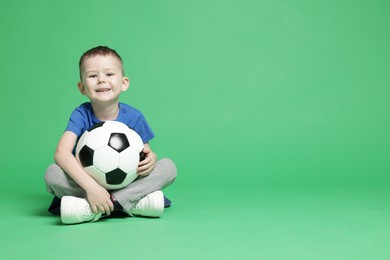 Photo of Cute little boy with soccer ball on green background, space for text