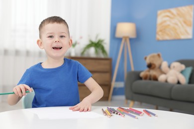 Photo of Cute little boy with green pencil at table indoors