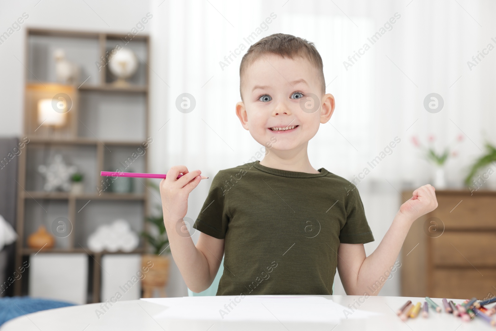 Cute little boy with pink pencil at table indoors Photo of Cute little boy with pink pencil at table indoors