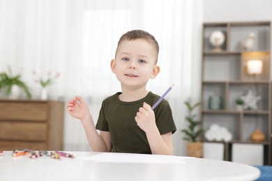 Photo of Cute little boy with violet pencil at table indoors