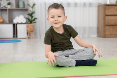 Photo of Cute little boy sitting on fitness mat at home