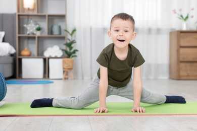 Photo of Cute little boy exercising on fitness mat at home