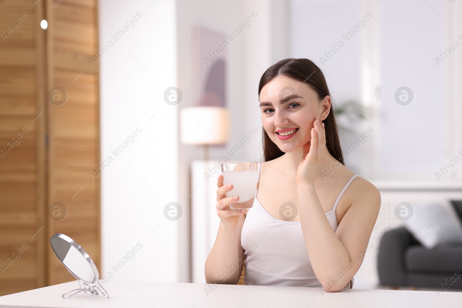 Smiling woman with glass of collagen water at table indoors Photo of Smiling woman with glass of collagen water at table indoors