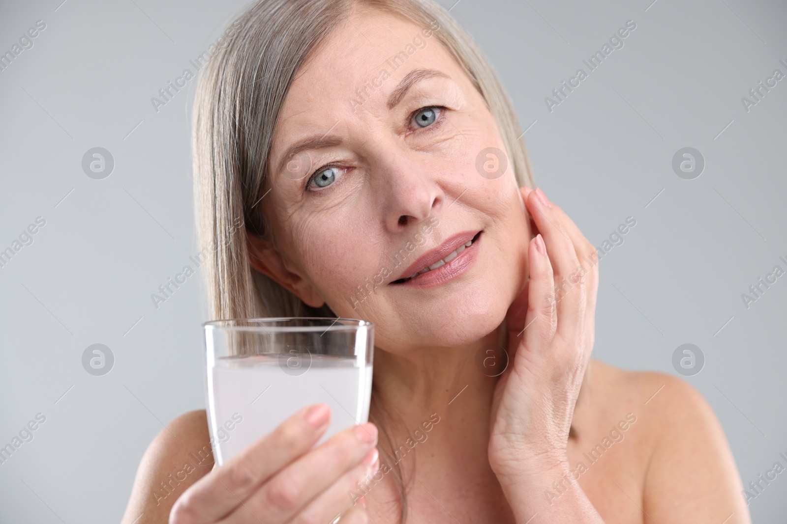 Woman with glass of collagen water on grey background Photo of Woman with glass of collagen water on grey background