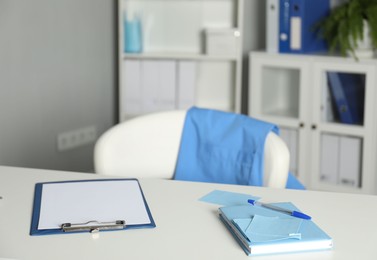 Photo of Doctor's workplace. Clipboard and other stationery on white table in medical office