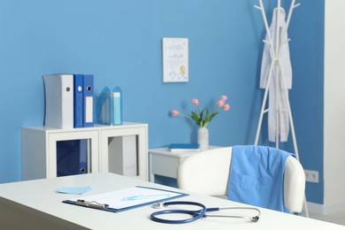 Photo of Doctor's workplace. Stethoscope, clipboard and other stationery on white table in medical office