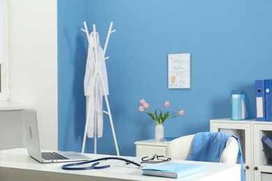 Photo of Doctor's workplace. Stethoscope, laptop, notebook and glasses on white table in medical office