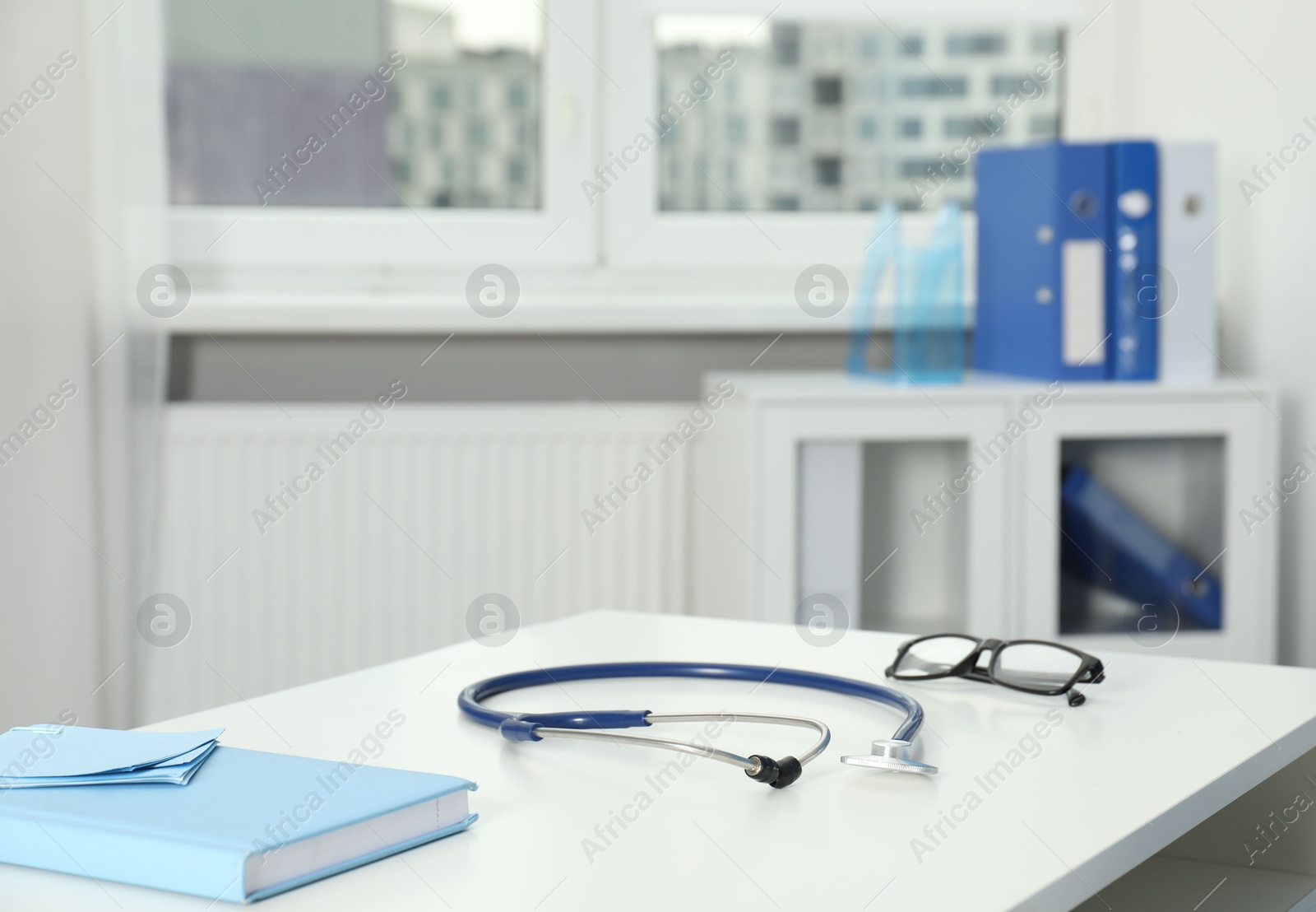 Doctor's workplace. Stethoscope, notebook and glasses on white table in medical office Photo of Doctor's workplace. Stethoscope, notebook and glasses on white table in medical office