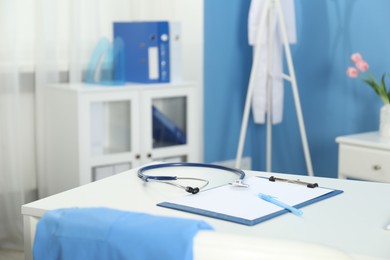 Photo of Doctor's workplace. Stethoscope, clipboard and pen on white table in medical office