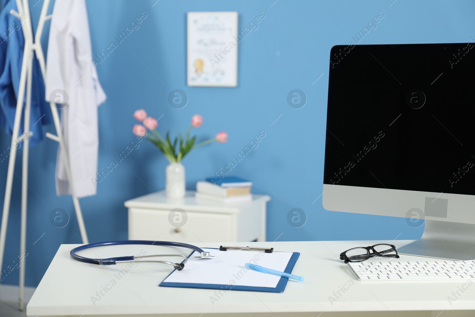 Doctor's workplace. Computer monitor, clipboard, stethoscope and glasses on white table in medical office Photo of Doctor's workplace. Computer monitor, clipboard, stethoscope and glasses on white table in medical office