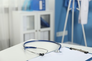 Photo of Doctor's workplace. Stethoscope and clipboard on white table in medical office, closeup. Space for text