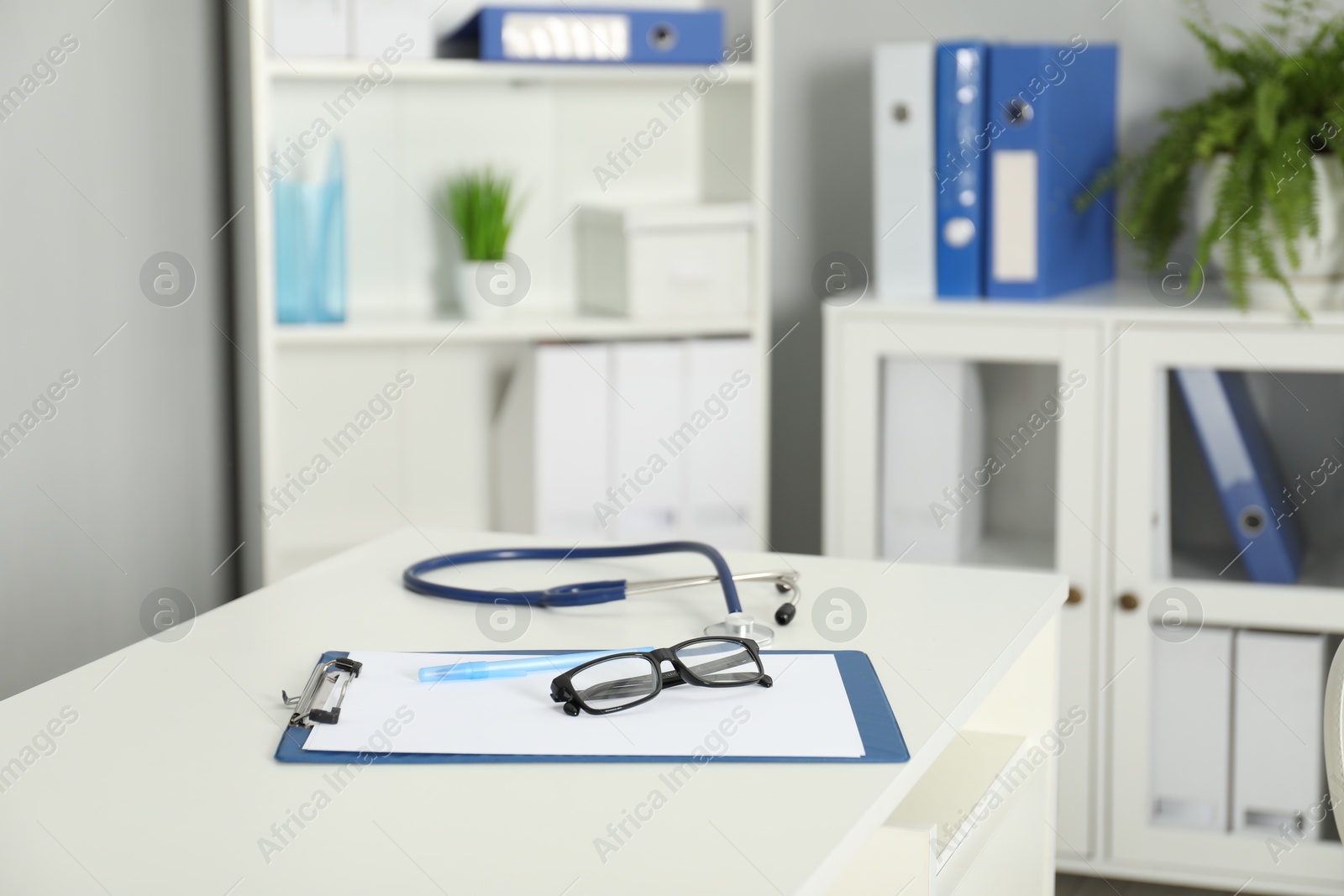 Doctor's workplace. Stethoscope, clipboard, pen and glasses on white table in medical office Photo of Doctor's workplace. Stethoscope, clipboard, pen and glasses on white table in medical office