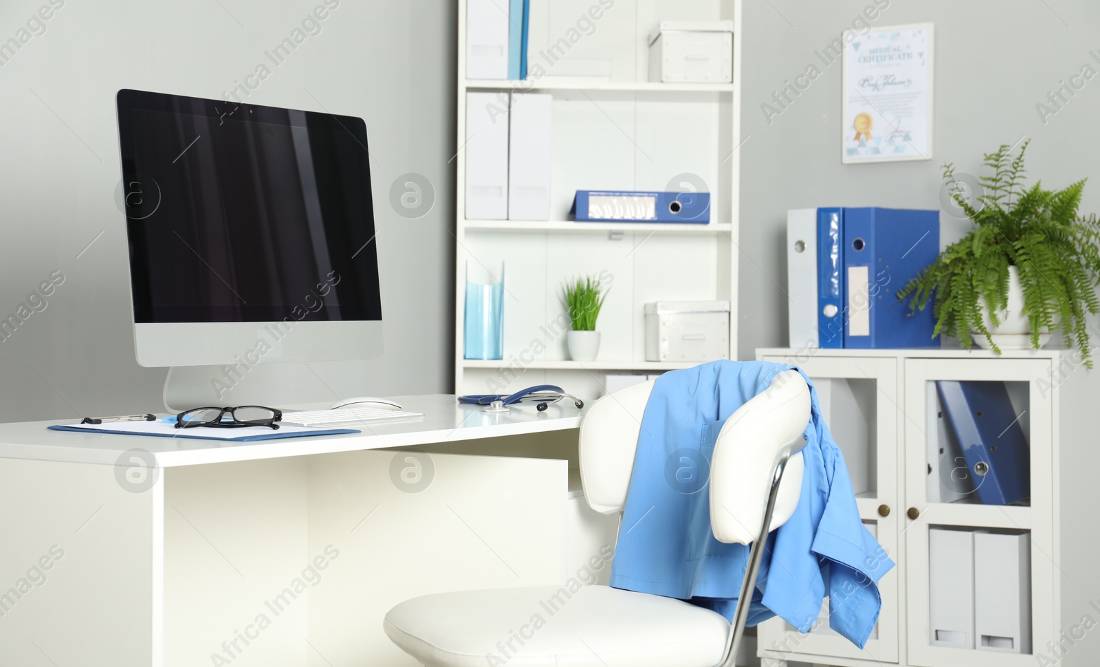 Doctor's workplace. Computer monitor, clipboard, stethoscope and glasses on white table in medical office Photo of Doctor's workplace. Computer monitor, clipboard, stethoscope and glasses on white table in medical office