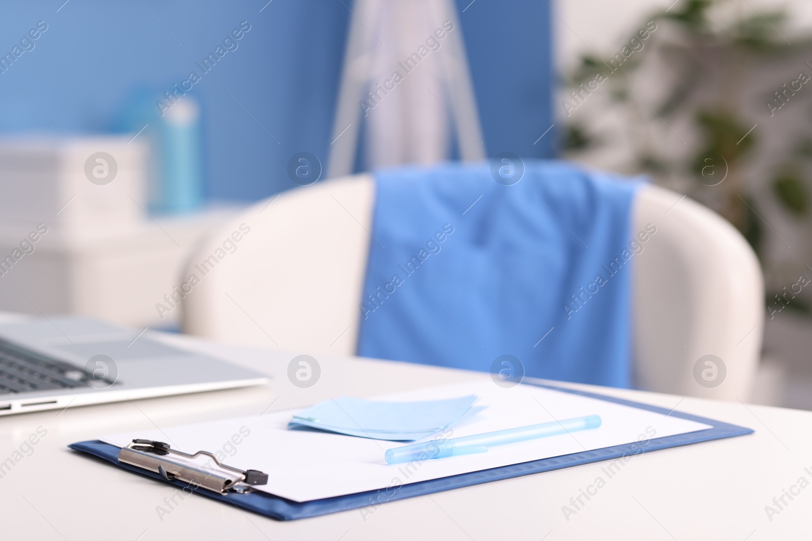 Photo of Doctor's workplace. Clipboard, other stationery and laptop on white table in medical office, closeup