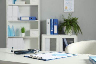 Photo of Doctor's workplace. Stethoscope, clipboard and other stationery on white table in medical office