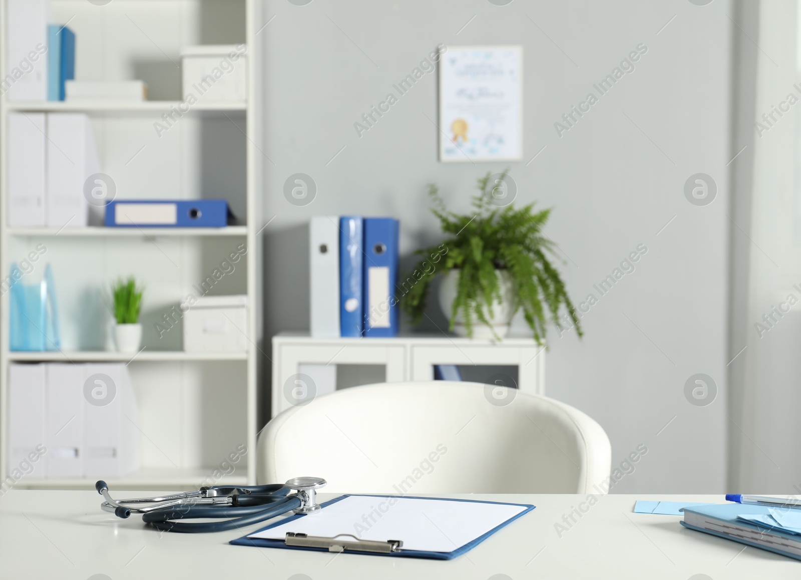 Doctor's workplace. Stethoscope, clipboard and other stationery on white table in medical office Photo of Doctor's workplace. Stethoscope, clipboard and other stationery on white table in medical office