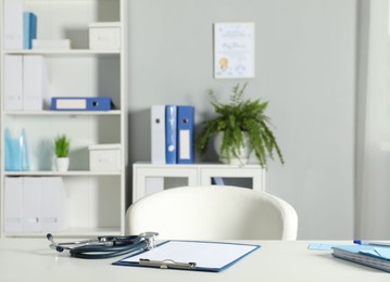 Photo of Doctor's workplace. Stethoscope, clipboard and other stationery on white table in medical office