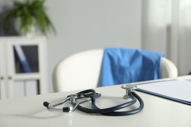 Photo of Doctor's workplace. Stethoscope and clipboard on white table in medical office, closeup. Space for text