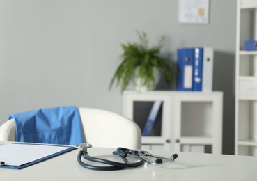 Photo of Doctor's workplace. Stethoscope and clipboard on white table in medical office