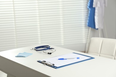 Photo of Doctor's workplace. Clipboard, other stationery and stethoscope on white table in medical office