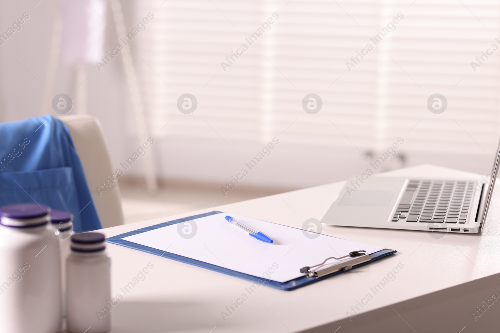 Doctor's workplace. Clipboard, pen, laptop and bottles of pills on white table in medical office Photo of Doctor's workplace. Clipboard, pen, laptop and bottles of pills on white table in medical office