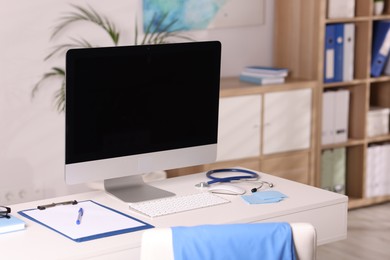 Photo of Doctor's workplace. Computer monitor, keyboard, mouse, stethoscope and stationery on white table in medical office