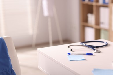 Photo of Doctor's workplace. Stethoscope, pen and sticky notes on white table in medical office, space for text