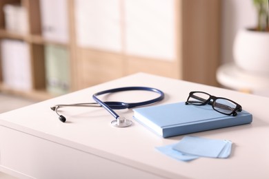 Photo of Doctor's workplace. Stethoscope, glasses and stationery on white table in medical office, closeup