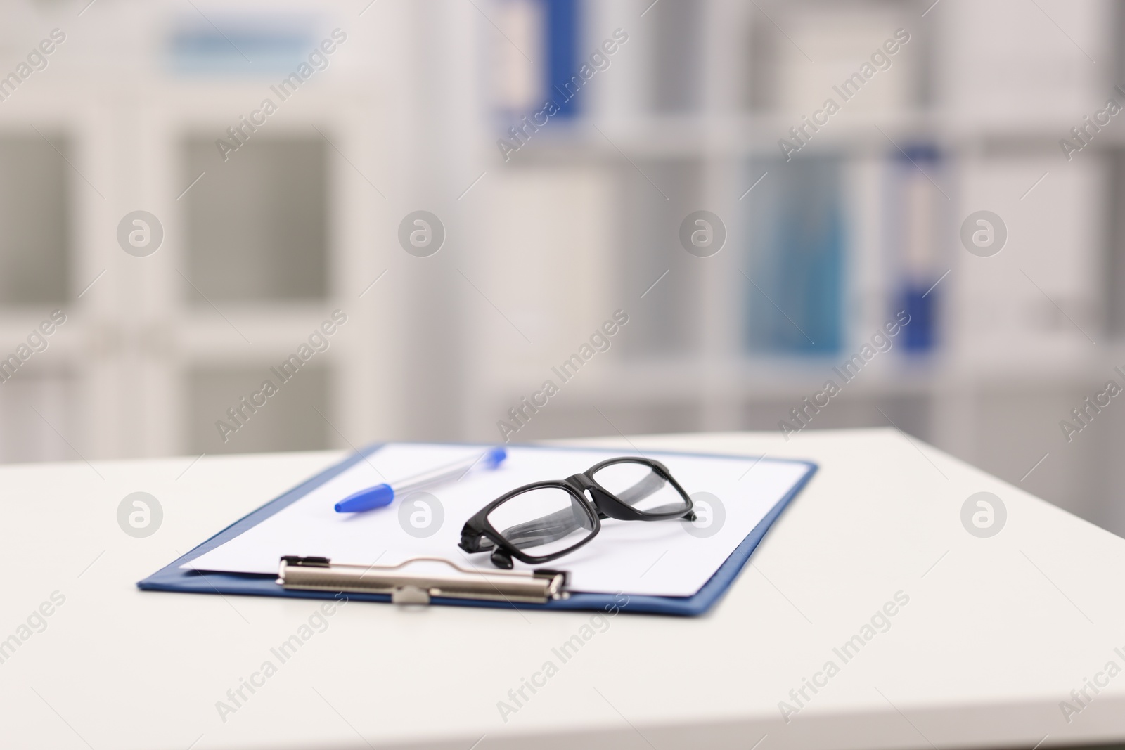Photo of Doctor's workplace. Clipboard, pen and glasses on white table in medical office, closeup. Space for text