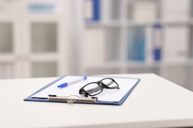 Photo of Doctor's workplace. Clipboard, pen and glasses on white table in medical office, closeup. Space for text