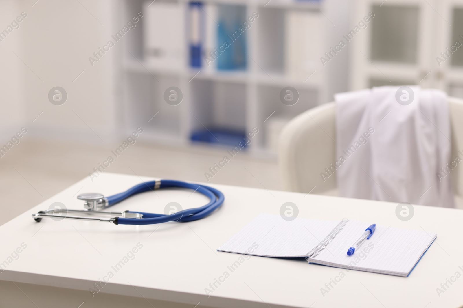 Doctor's workplace. Stethoscope, open notebook and pen on white table in medical office, space for text Photo of Doctor's workplace. Stethoscope, open notebook and pen on white table in medical office, space for text
