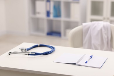 Photo of Doctor's workplace. Stethoscope, open notebook and pen on white table in medical office, space for text
