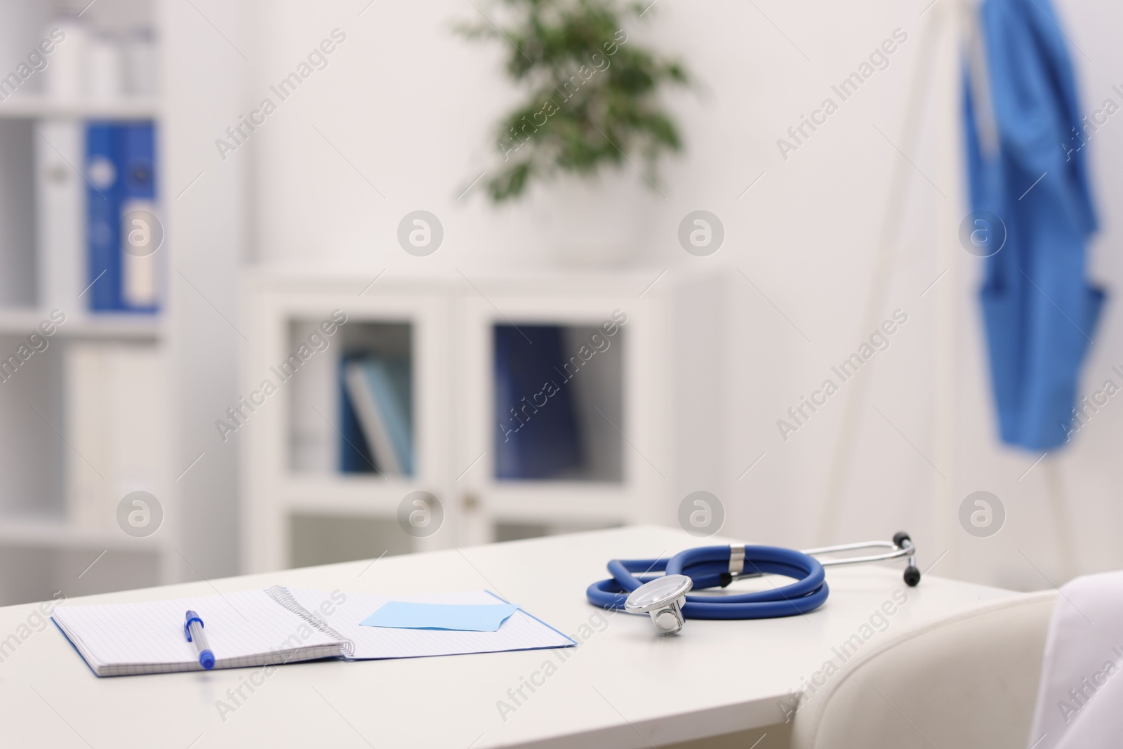 Doctor's workplace. Open notebook, pen, sticky notes and stethoscope on white table in medical office, space for text Photo of Doctor's workplace. Open notebook, pen, sticky notes and stethoscope on white table in medical office, space for text