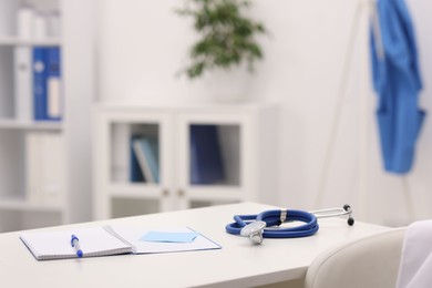 Photo of Doctor's workplace. Open notebook, pen, sticky notes and stethoscope on white table in medical office, space for text