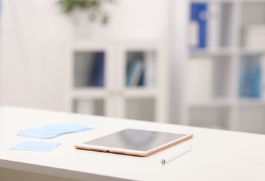 Photo of Doctor's workplace. Tablet, pen and sticky notes on white table in medical office, closeup. Space for text