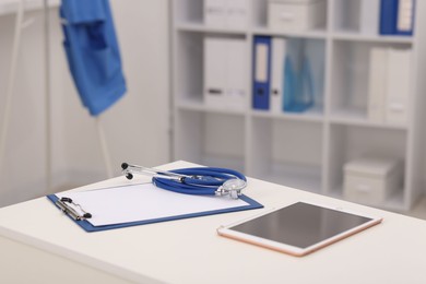 Photo of Doctor's workplace. Tablet, clipboard and stethoscope on white table in medical office