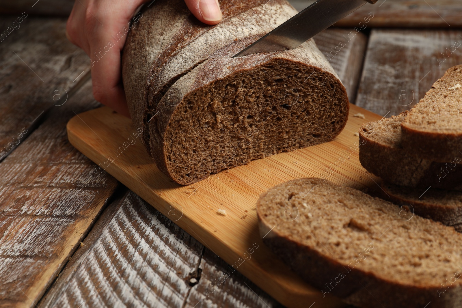 Woman cutting fresh bread at wooden table, closeup Photo of Woman cutting fresh bread at wooden table, closeup