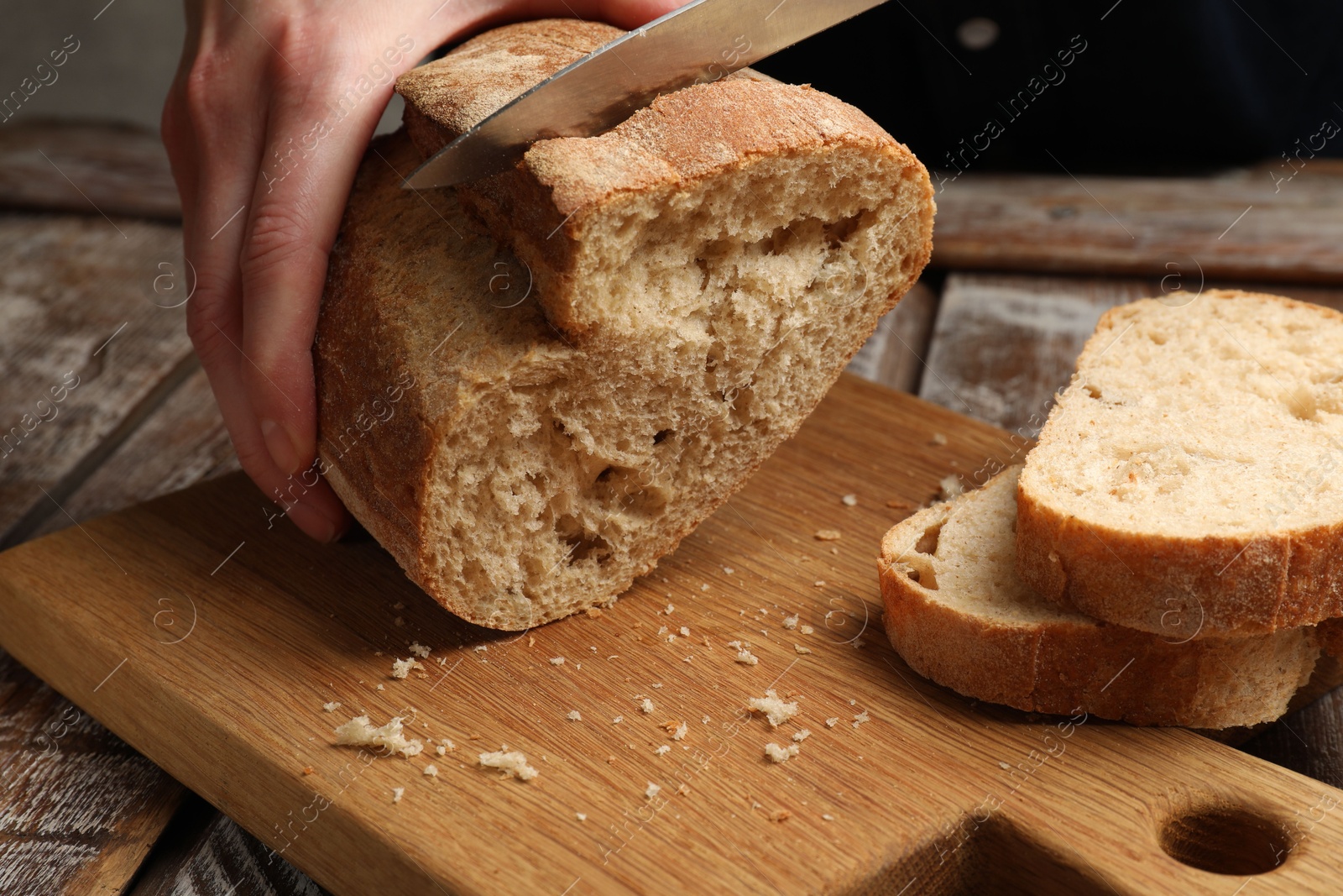 Photo of Woman cutting fresh bread at wooden table, closeup