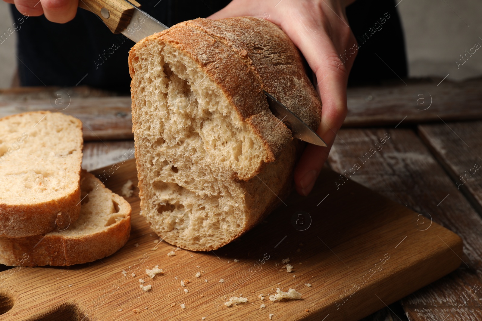 Woman cutting fresh bread at wooden table, closeup Photo of Woman cutting fresh bread at wooden table, closeup